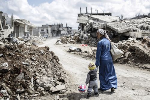 A Kurdish Syrian woman walks with her child past the ruins of the town of Kobane, also known as Ain al-Arab by Yasin Akgül